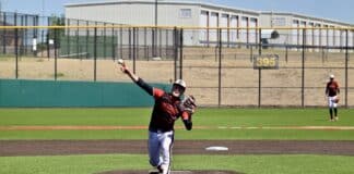 Baseball pitcher in red and black uniform throws from the mound on a sunny field.