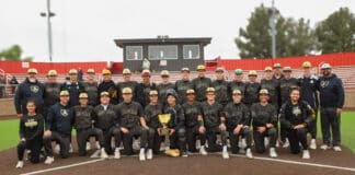 Baseball team posing for a group photo on the field with a trophy at center.