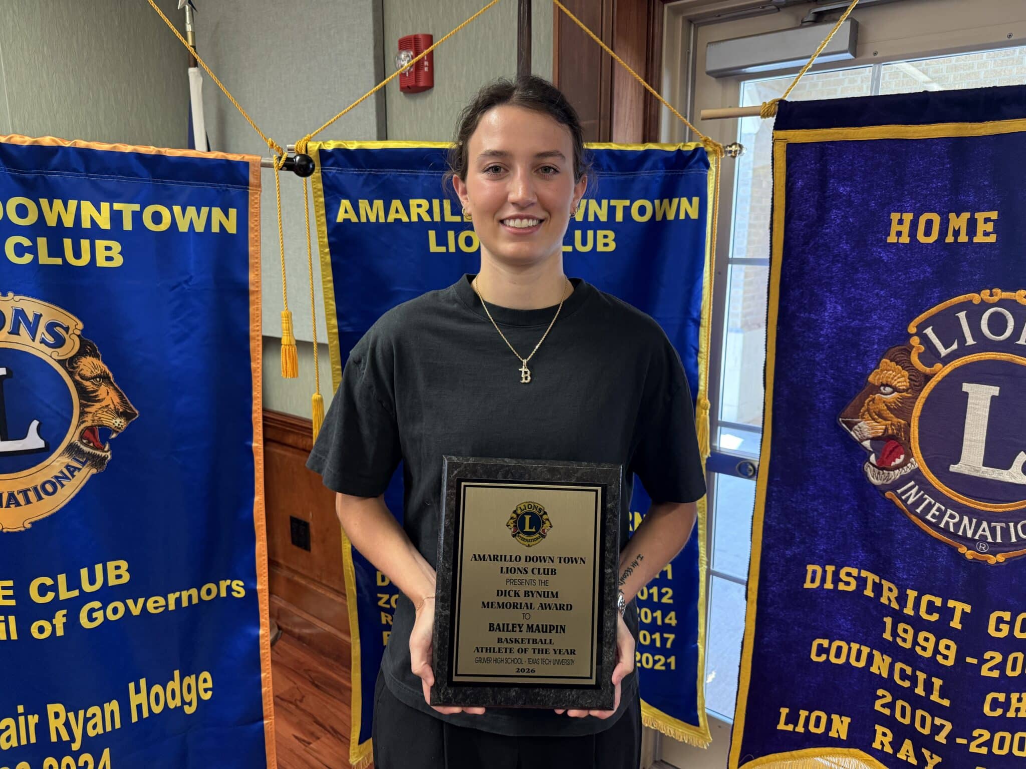 IMG_5326 | Press Pass Sports Young woman standing in front of Amarillo Downtown Lions Club banners, holding a framed award plaque.