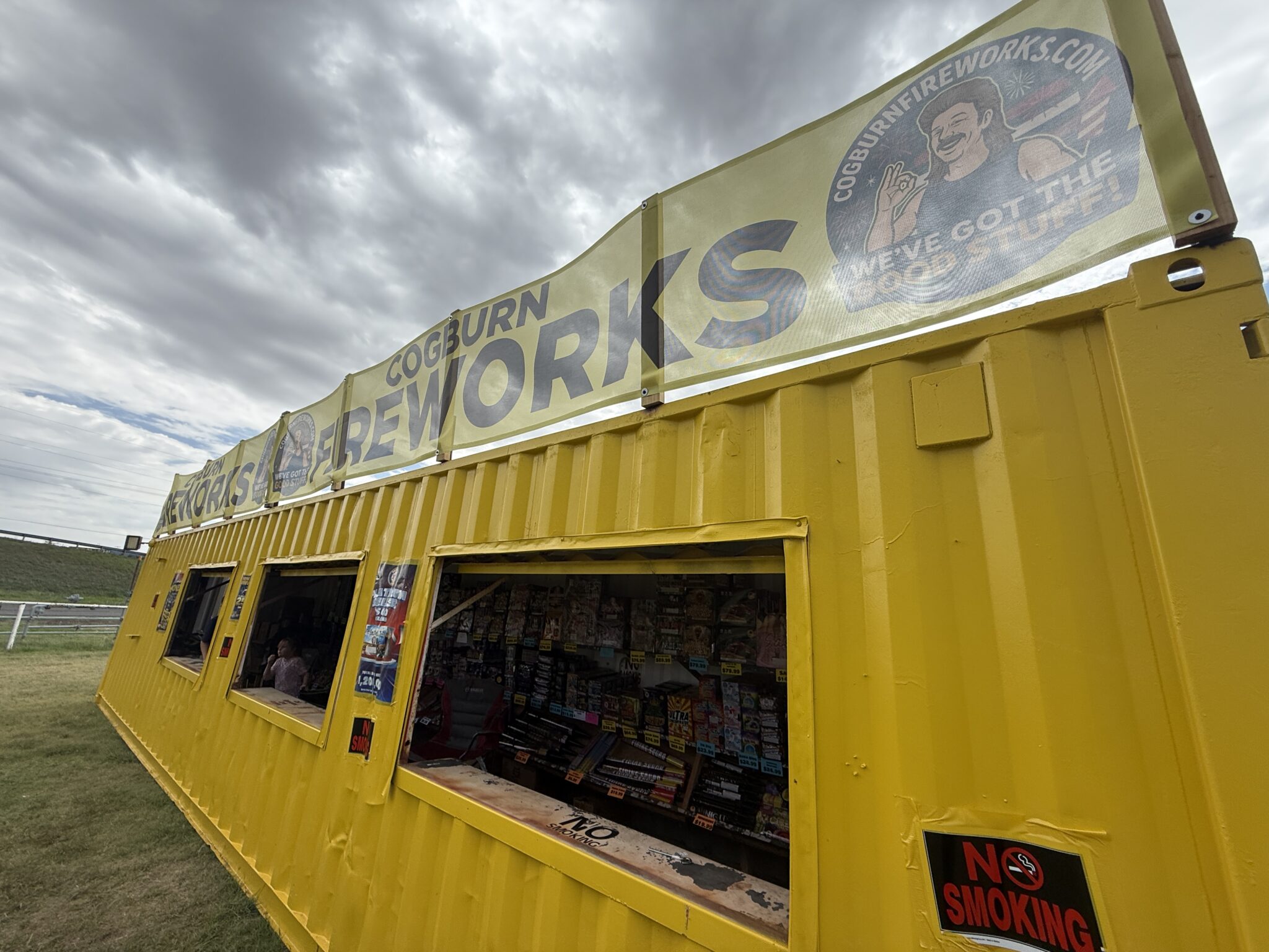 Bright yellow kiosk with open storefront windows selling magazines, against a cloudy sky.
