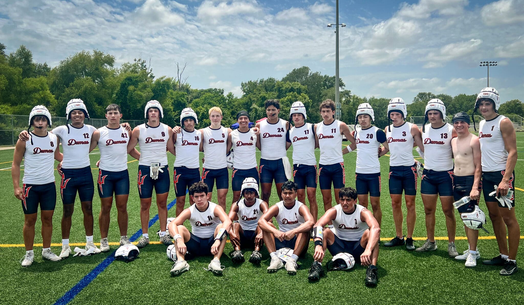 image | Press Pass Sports Group of male lacrosse players in white Dumas jerseys posing together on a field, wearing helmets and shorts.